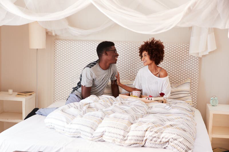 Tausendjähriger Afroamerikanermann, der sein Partnerfrühstück und -geschenke im Bett gibt, um zu feiern stockbilder