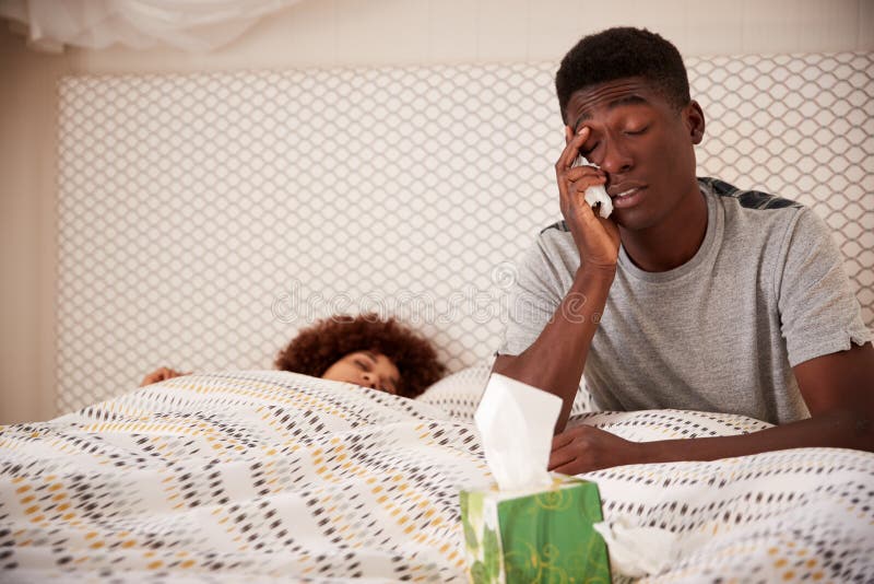 Tausendjähriger Afroamerikanermannkranke im Bett, oben sitzend, während Partner neben ihm schläft, nah oben lizenzfreies stockfoto