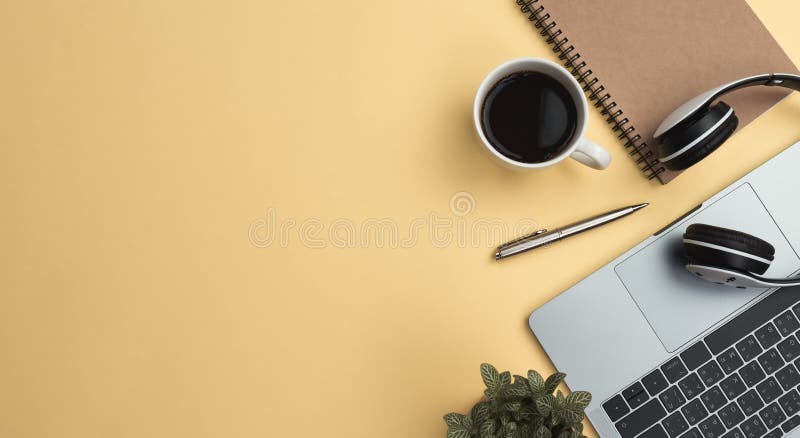 tavola dello scrittorio di giallo dell'area di lavoro dell'ufficio con il computer portatile, caffè, cellulare, taccuino, pianta