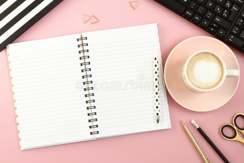 Tavola rosa della scrivania con il taccuino, la tazza di caffè, la penna, la matita, le forbici ed il computer aperti fotografia stock libera da diritti