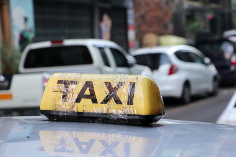 Taxi light sign or cab sign in yellow color with black text and tied with transparent tape on the car roof at the street blurred