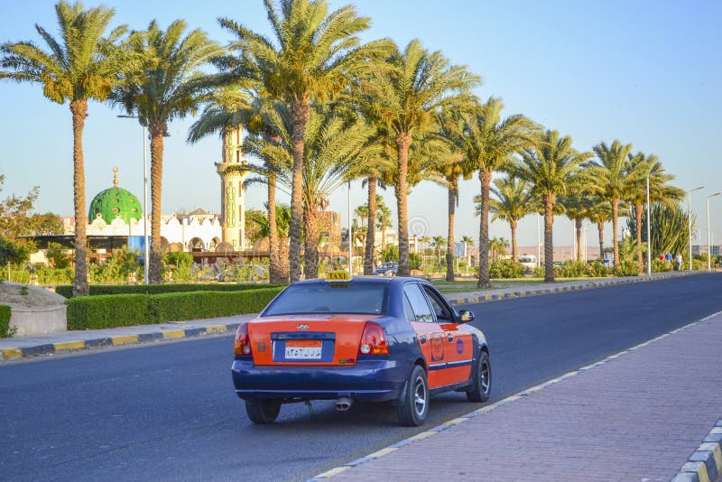 Hurghada, Egypt - may 15th 2018: Egyptian taxi blue-orange colour goes on the road at the resort area of Hurghada. A sidewalk, a mosque and palm trees along the road in the background. Hurghada, Egypt - may 15th 2018: Egyptian taxi blue-orange colour goes on the road at the resort area of Hurghada. A sidewalk, a mosque and palm trees along the road in the background.