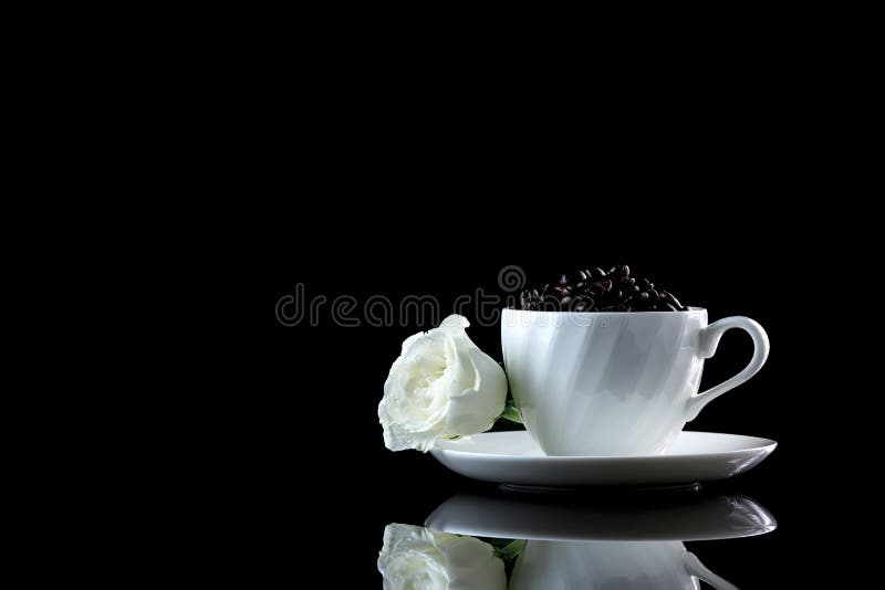 Taza con los granos de café y la rosa del blanco en un backgr reflexivo negro fotos de archivo libres de regalías Taza con los granos de café y la rosa del blanco en un backgr reflexivo negro fotos de archivo libres de regalías