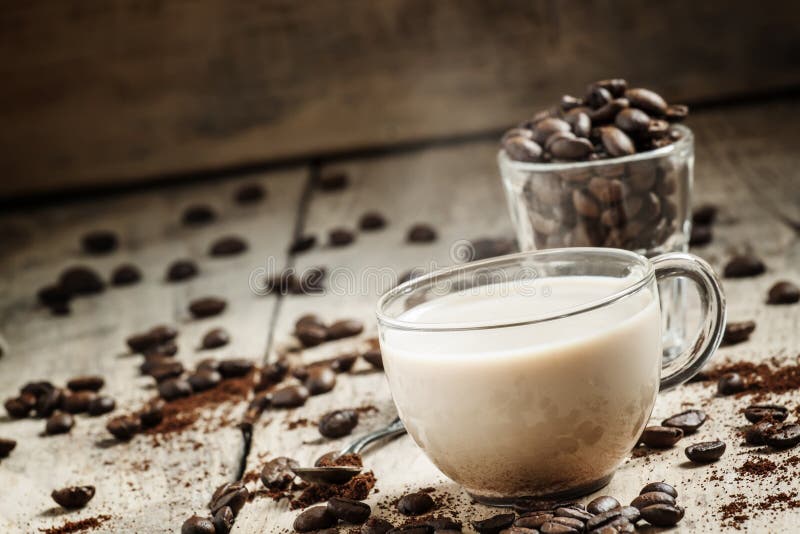 Taza de café de cristal con la leche, el grano derramado y el café molido o foto de archivo libre de regalías Taza de café de cristal con la leche, el grano derramado y el café molido o foto de archivo libre de regalías