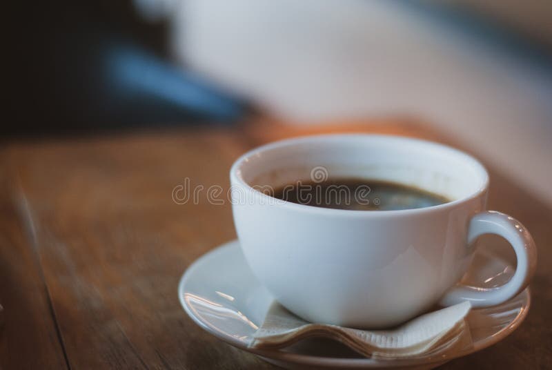 Taza de café llenada del café de Americano en la placa con el papel seda marrón en la tabla de madera del vintage
