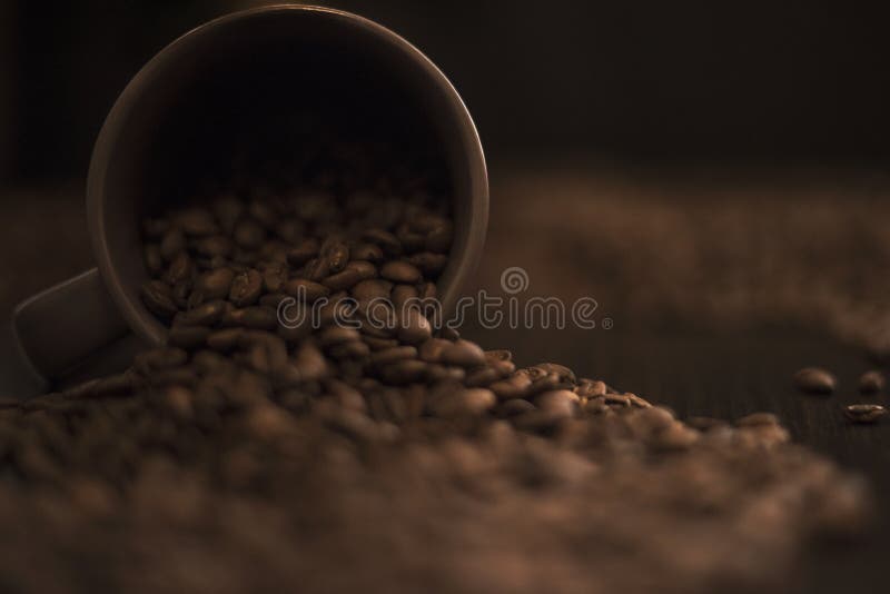 Taza de café marrón volcada y granos de café asados en la tabla de cocina oscura foto de archivo