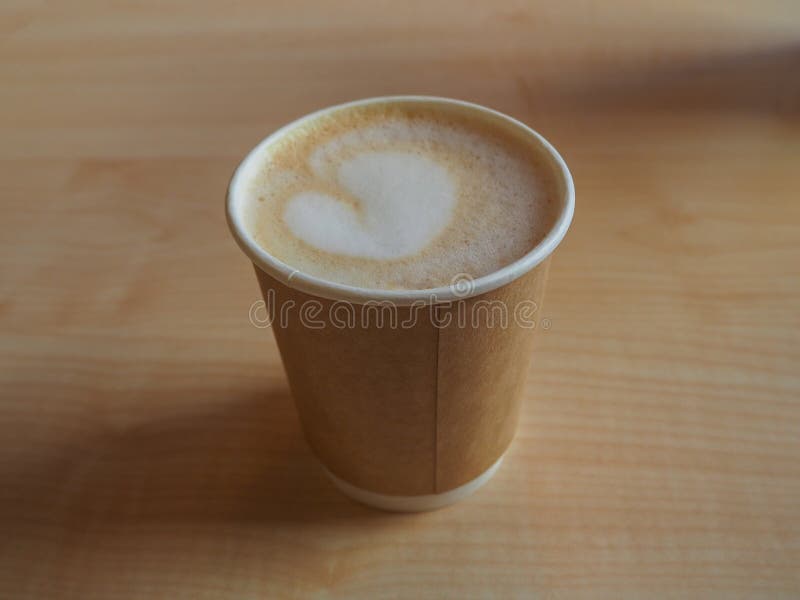 Taza de capuchino en la taza para llevar de papel en la tabla de madera foto de archivo libre de regalías Taza de capuchino en la taza para llevar de papel en la tabla de madera foto de archivo libre de regalías