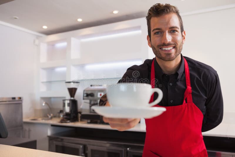 Taza de ofrecimiento del barista feliz de café a la cámara imagenes de archivo Taza de ofrecimiento del barista feliz de café a la cámara imagenes de archivo