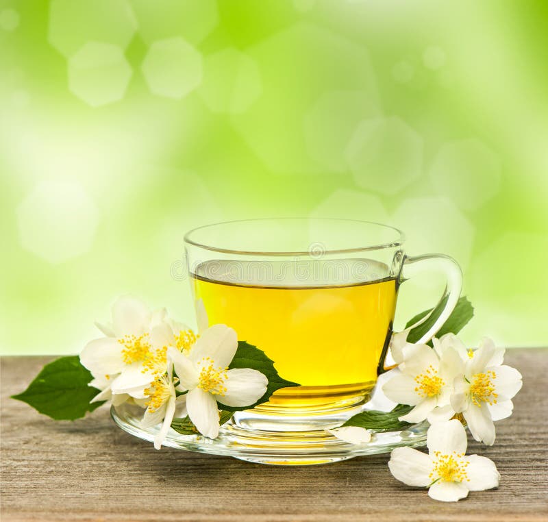Cup of tea with jasmine flowers on wooden table over blurred green background. Cup of tea with jasmine flowers on wooden table over blurred green background