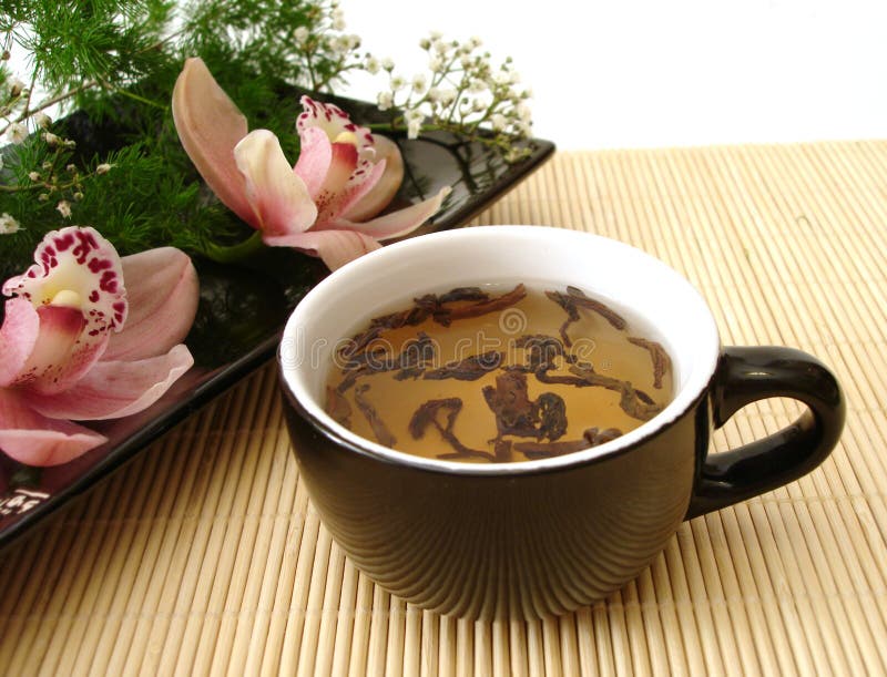 Taza de té con las orquídeas rosadas en la placa negra sobre la paja mate imagen de archivo libre de regalías Taza de té con las orquídeas rosadas en la placa negra sobre la paja mate imagen de archivo libre de regalías