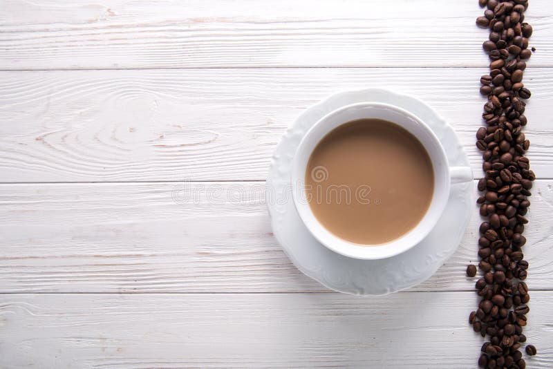 Tazza di caffè bianca con latte o tè al latte su fondo di legno bianco decorato con i chicchi di caffè fotografia stock Tazza di caffè bianca con latte o tè al latte su fondo di legno bianco decorato con i chicchi di caffè fotografia stock