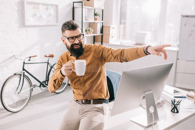 Tazza di caffè della tenuta dell'uomo d'affari e dito adulti barbuti felici indicare in exitement immagine stock Tazza di caffè della tenuta dell'uomo d'affari e dito adulti barbuti felici indicare in exitement immagine stock