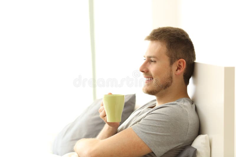 Tazza di caffè felice della tenuta dell'uomo sul letto fotografie stock Tazza di caffè felice della tenuta dell'uomo sul letto fotografie stock
