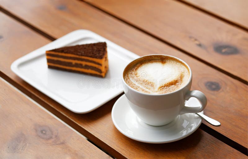 Tazza di cappuccino e pezzo di dolce a strisce su una tavola di legno fotografia stock libera da diritti Tazza di cappuccino e pezzo di dolce a strisce su una tavola di legno fotografia stock libera da diritti