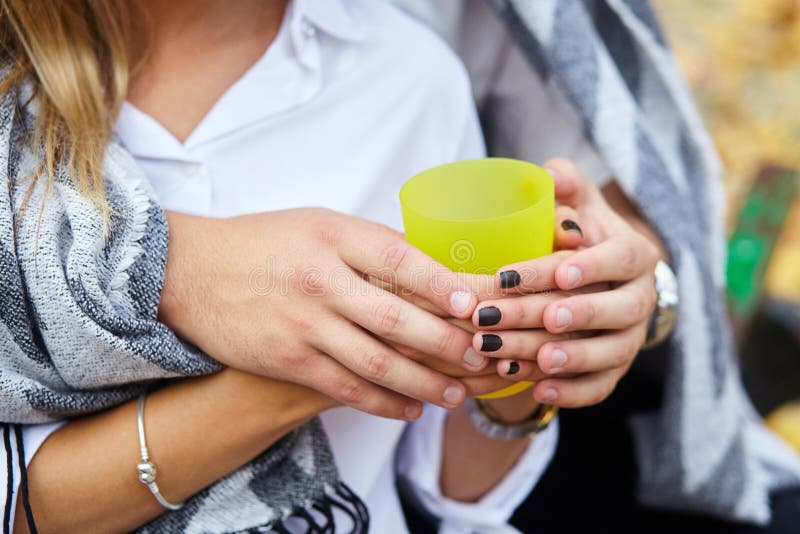 Tazza gialla di tè caldo in mani dell'amante Giovani coppie immagine stock