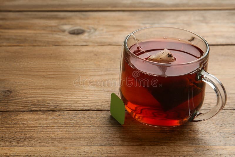 Tea Bag in Glass Cup of Hot Water on Wooden Table. Space for Text Stock