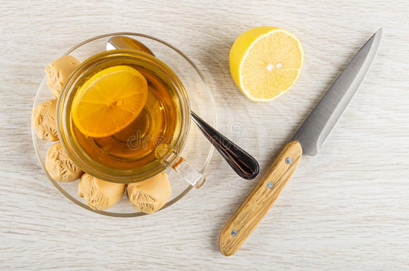 Tea with lemon in cup, creamy fudge, spoon on saucer, piece of lemon, knife on wooden table. Top view