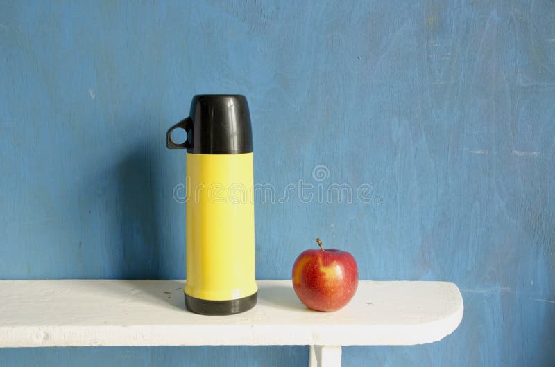 Tea thermos and red apple on wooden shelf