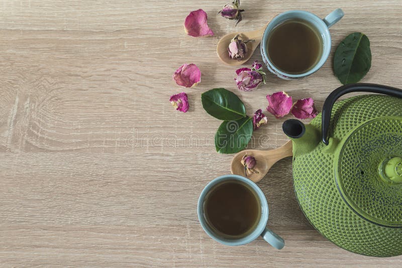 Tea time concept. Green iron tea pot, two cup of tea, rose buds and petals, leaves