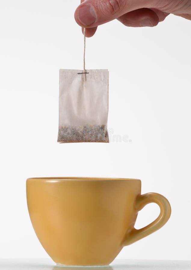 Soaking a tea bag on a yellow cup,Tea bag on cup.Holding tea bag. Soaking a tea bag on a yellow cup,Tea bag on cup.Holding tea bag.