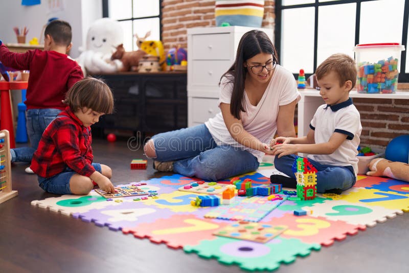 Teacher with Boys Playing with Maths Puzzle Game Sitting on Floor at Kindergarten Stock Image