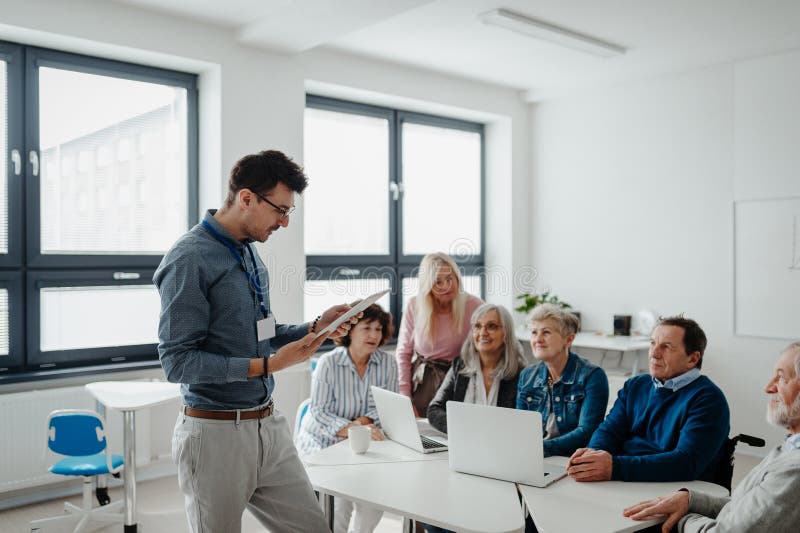 Teacher explaining senior students how to work with laptop and internet. Elderly people attending computer and stock photo