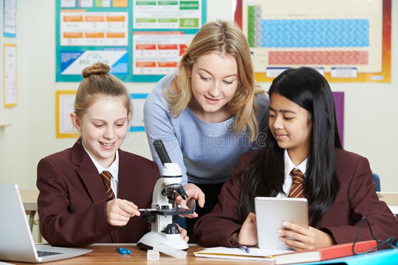 Teacher with Female Students Using Microscope in Science Class Stock