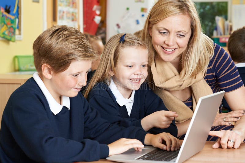 Teacher Helping Elementary School Pupils In Computer Class