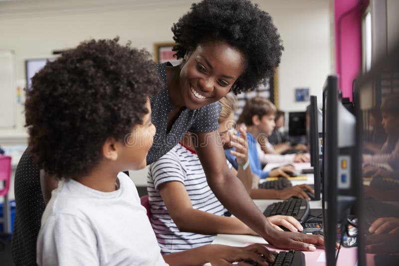 Teacher Helping Male Pupil Line Of High School Students Working at Screens In Computer Class