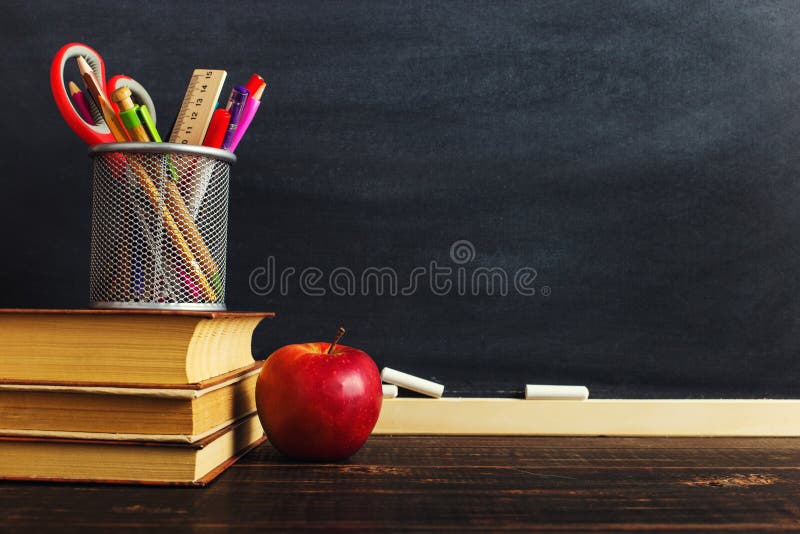 Teacher`s desk with writing materials, a book and an apple, a blank for text or a background for a school theme. Copy space