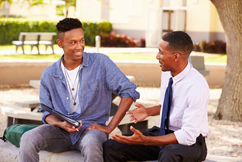 Teacher Sitting Outdoors Helping Male Student With Work stock photo Teacher Sitting Outdoors Helping Male Student With Work stock photo
