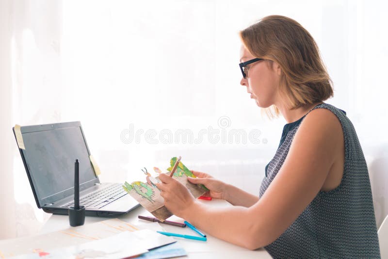 Teacher or speech therapist at work. Young woman with glasses sitting at the table and working with materials for children. Nearby