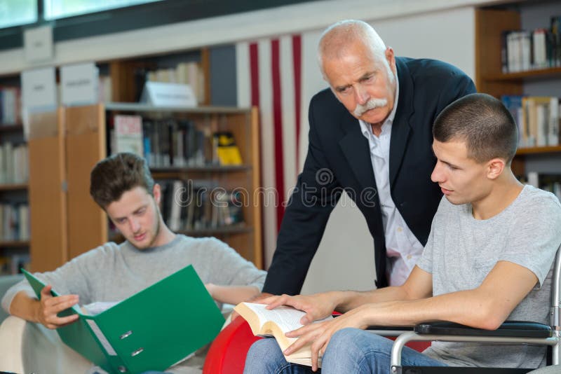 Teacher student in wheelchair working with classmate in library stock photos