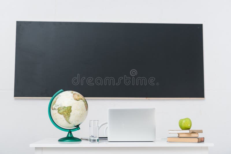 Teachers desk with laptop in classroom in front of chalkboard