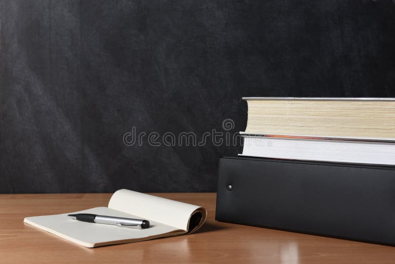 Teachers desk with note pad and pen and books stacked on a binder