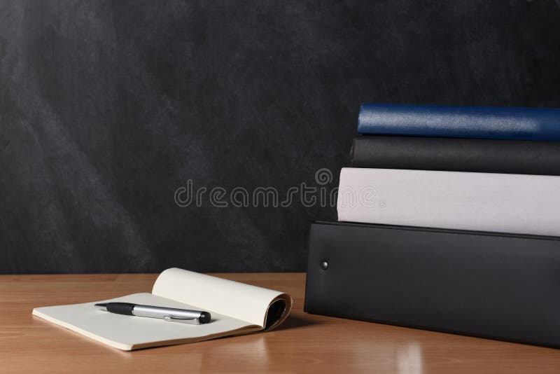Teachers desk with note pad and pen and a stack of binders and books