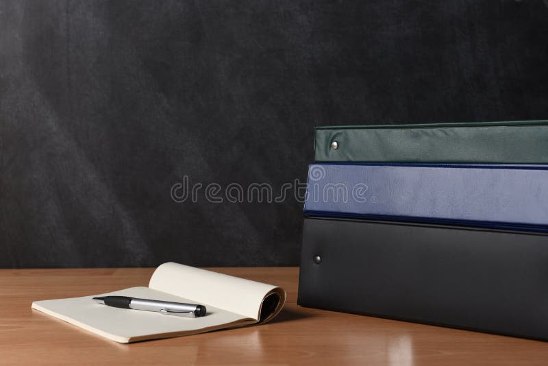 Teachers desk with note pad and pen and a stack of different colored binders