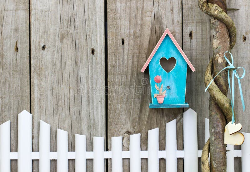 Teal blue birdhouse hanging over white picket fence
