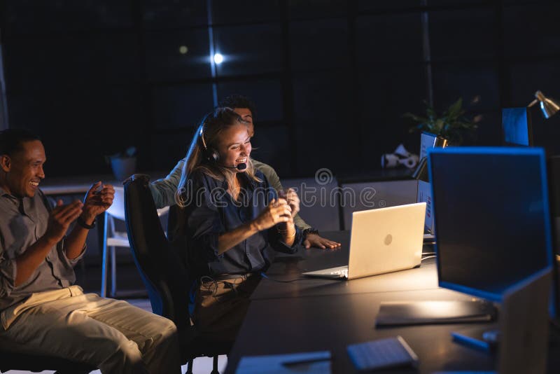 Team celebrating success at office, using laptops and headsets during night work stock photo