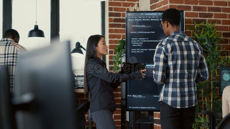 Team of coders analyzing code on wall screen tv comparing errors using digital tablet royalty free stock image