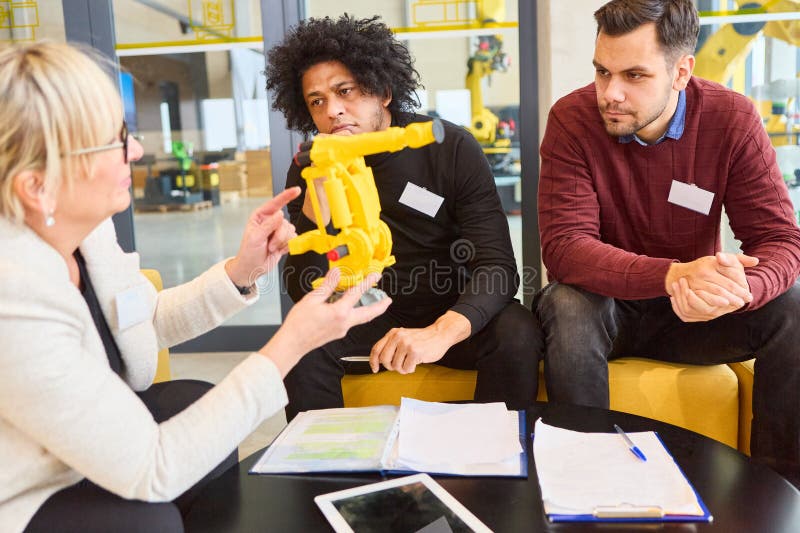 Team discussing robotics development and automation with a gripper arm model in office setting royalty free stock photography