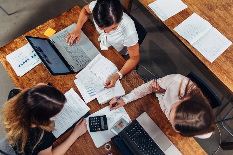 Team of female accountants preparing annual financial report working with papers using laptops sitting at desk in office stock photos Team of female accountants preparing annual financial report working with papers using laptops sitting at desk in office stock photos