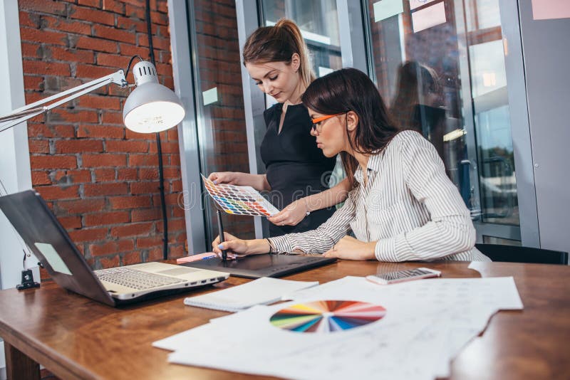 Team of female interior designer drawing a new project using graphic tablet, laptop and color palette sitting at desk in royalty free stock image