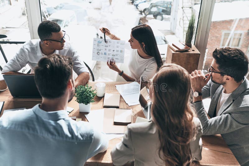 Team of innovators. Top view of young modern people in smart casual wear discussing business while working in the creative office stock image Team of innovators. Top view of young modern people in smart casual wear discussing business while working in the creative office stock image