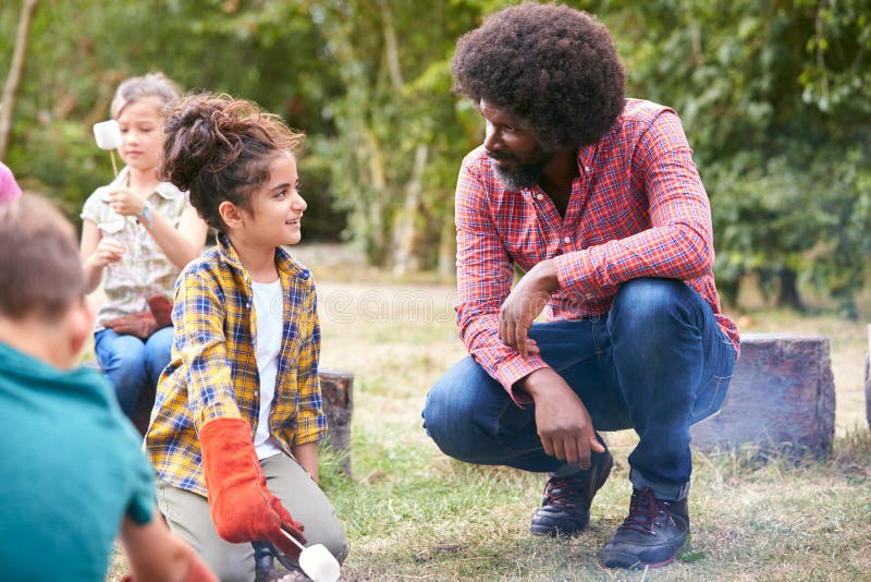 Team Leader With Group Of Children On Outdoor Activity Trip Toasting Marshmallows Over Camp Fire