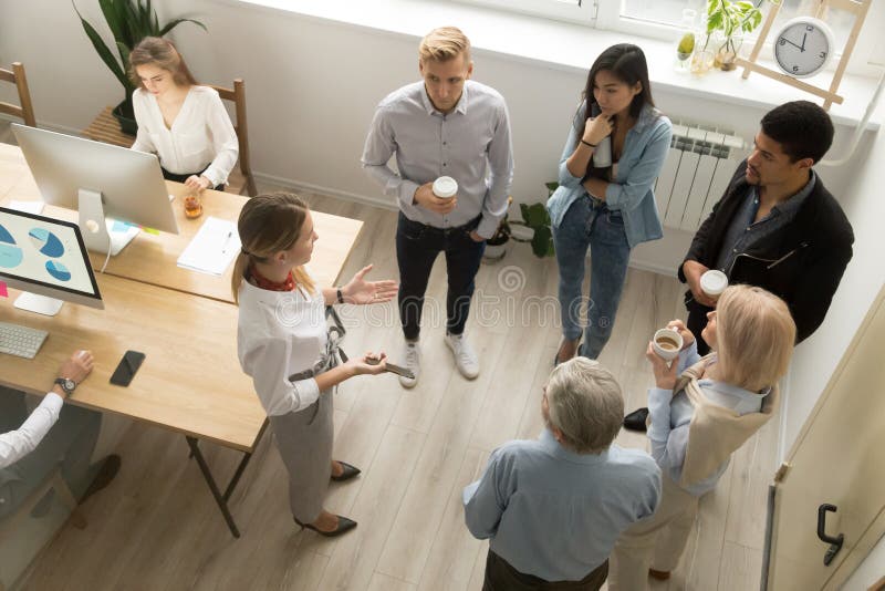 Team leaders meet multiracial interns in office explaining new job, company executives talking to diverse workers listening instructions at break, discussion and computer work in coworking, top view. Team leaders meet multiracial interns in office explaining new job, company executives talking to diverse workers listening instructions at break, discussion and computer work in coworking, top view