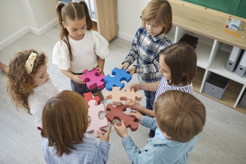 Team of school children standing in classroom and joining pieces of jigsaw puzzle