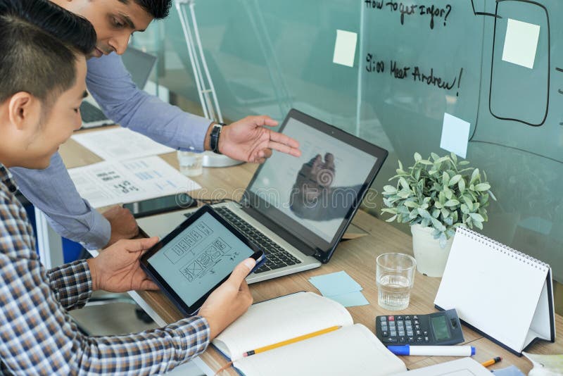 Team of UI designers working on interface of new mobile application and comparing layouts on screen of tablet computer and laptop