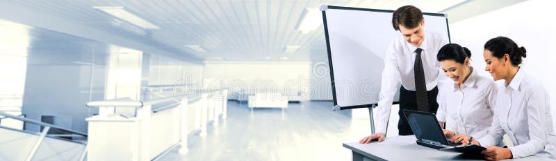 Two smiling business ladies sitting at table and looking at laptop monitor while their partner standing near by. Two smiling business ladies sitting at table and looking at laptop monitor while their partner standing near by