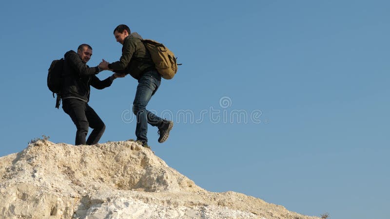 Teamwork of business people. tourists give hand to each other, climbing to top of hill. team of male travelers goes to victory and success. two climbers climb one after another on white rock. Teamwork of business people. tourists give hand to each other, climbing to top of hill. team of male travelers goes to victory and success. two climbers climb one after another on white rock.